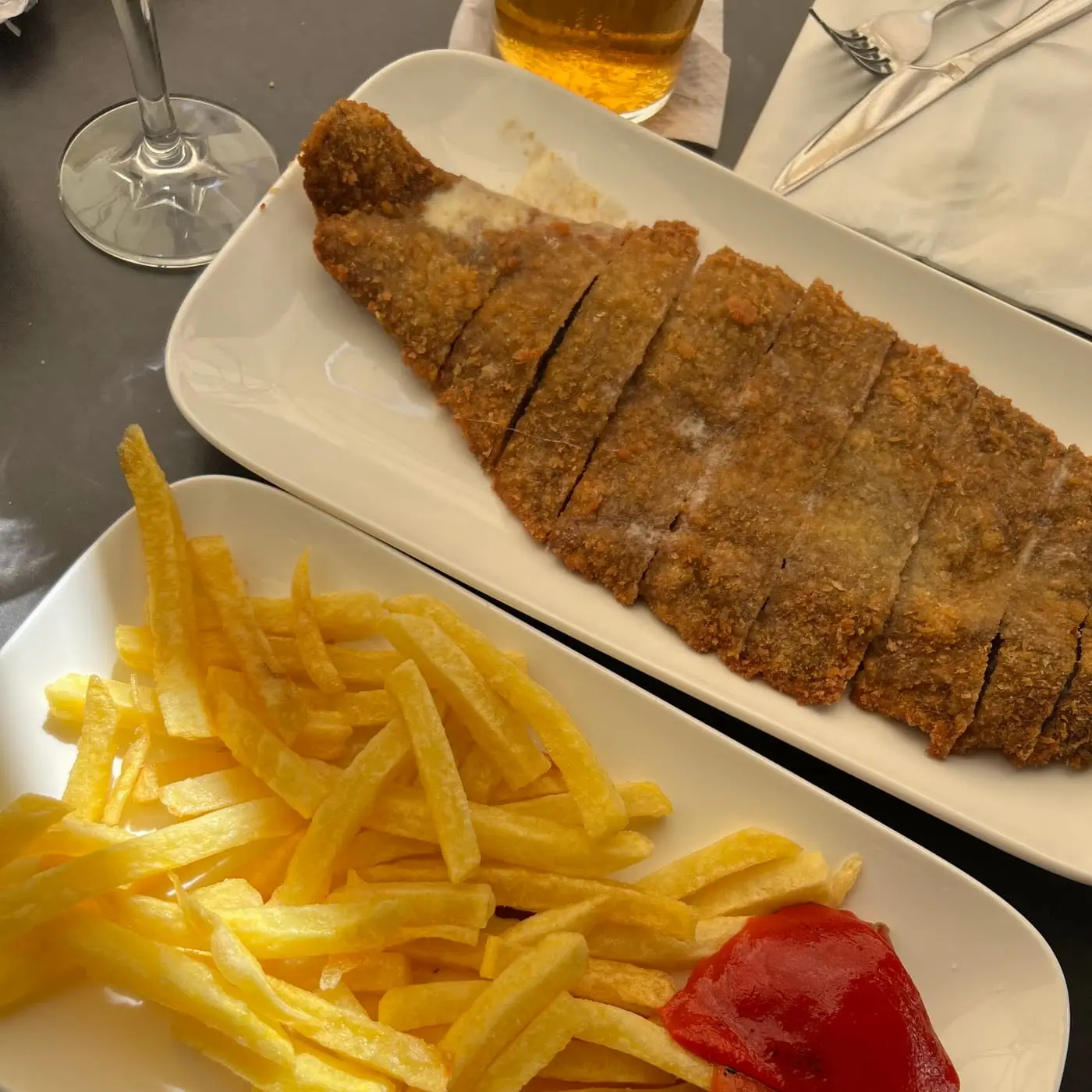 Cachopo empanado fileteado con patatas fritas y salsa en la mesa de El Gallu, con una copa de sidra al lado