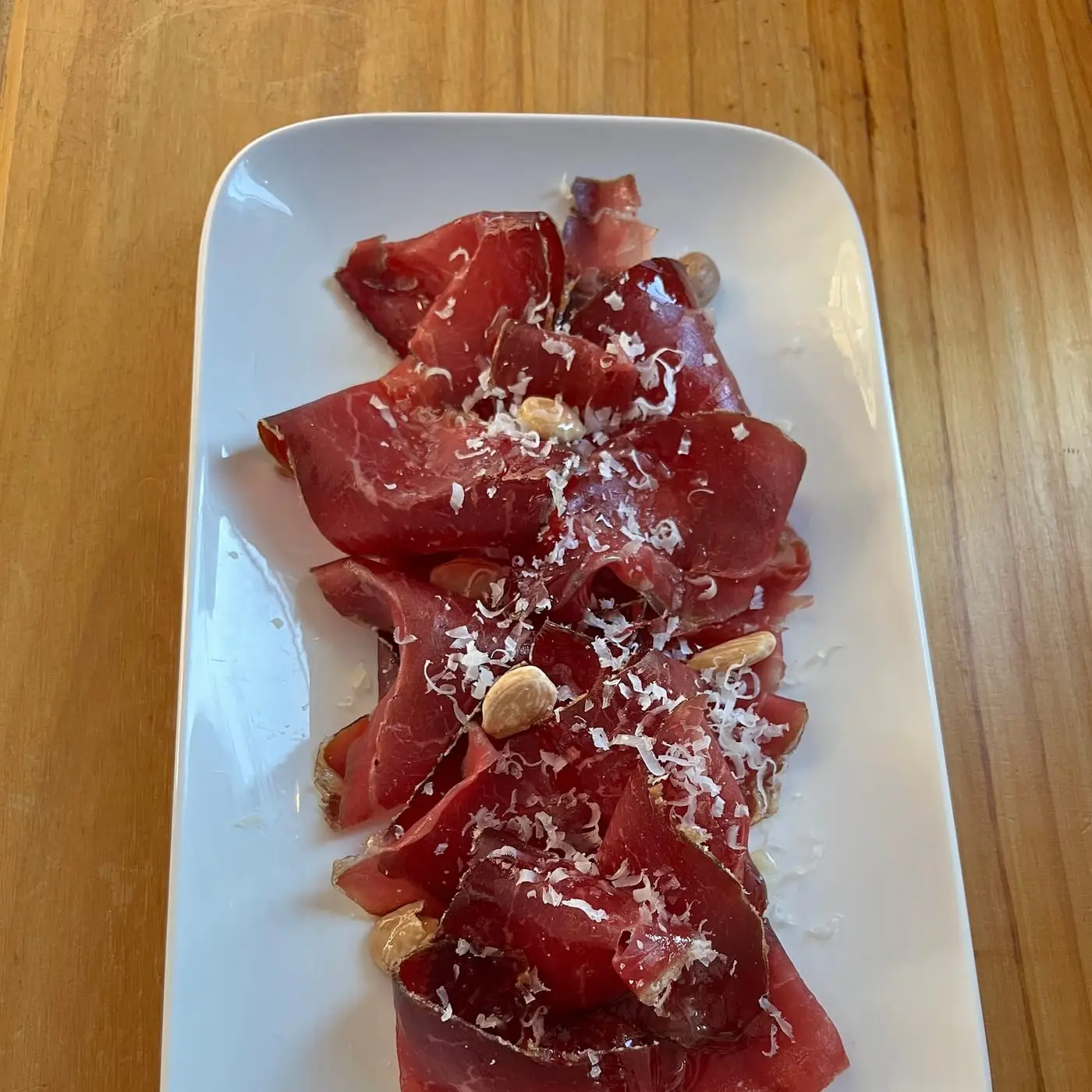 Carpaccio de vacuno con queso rallado y alcaparras sobre plato blanco